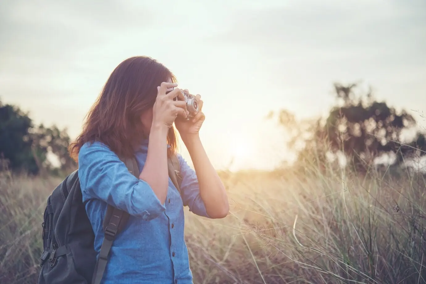 Junge Hipster-Frau macht Fotos mit einer Vintage-Filmkamera auf einem Sommerfeld. Frauen-Lifestyle-Konzept.